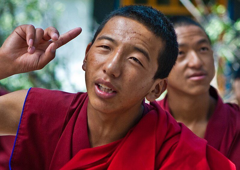 Tibetan_buddhist_monk_during_monastic_debate_making_hand_gesture_at_Sera_Monastery,_Lhasa,_Tibet_on_3_August_2008_(cropped)